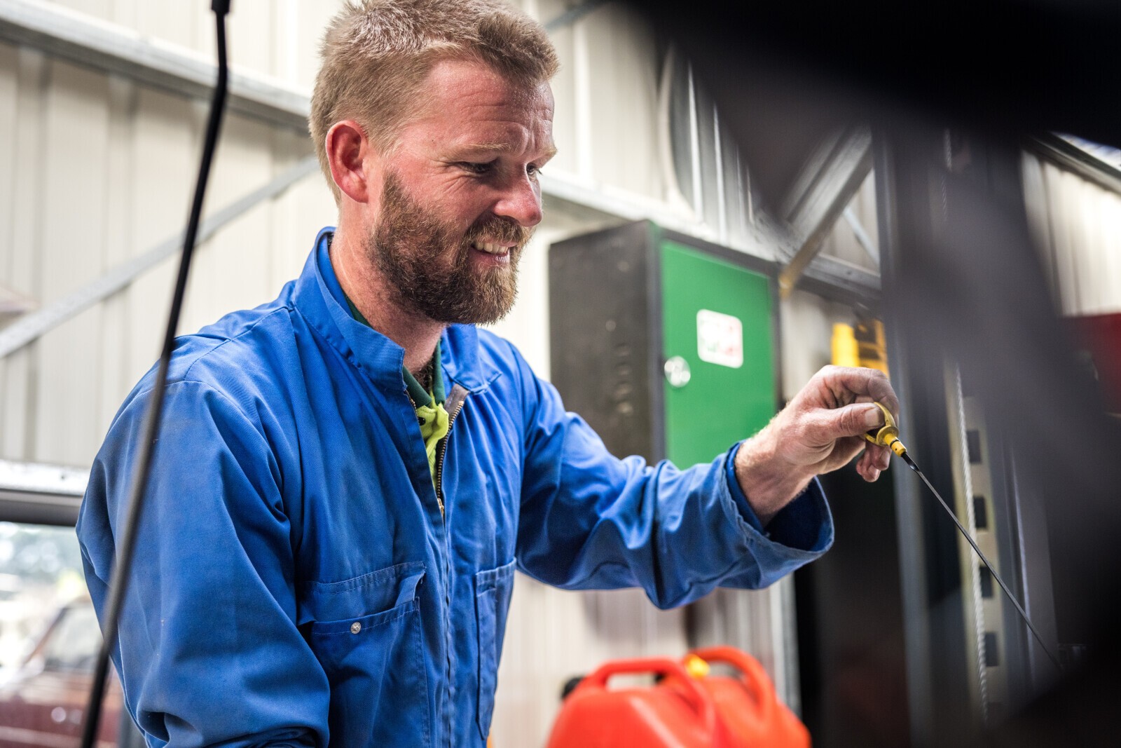 A mechanic in workshop overalls checking a dipstick